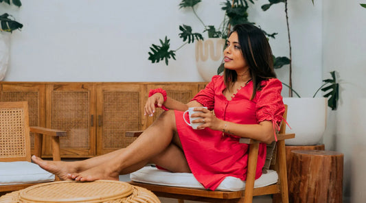 A woman sitting on a chair with a white cup of coffee wearing a red embroidered dress