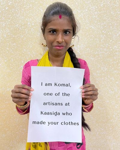 A female artisan holding up a banner that says "I am Komal, one of the artisans at Kaasida who made your clothes'.