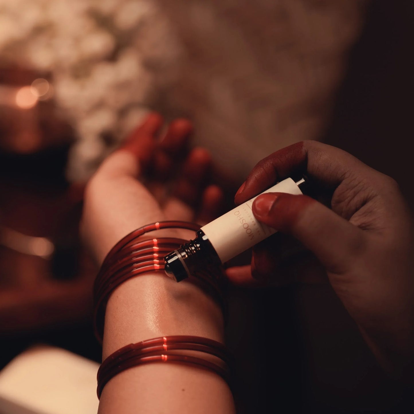 Close-up of a women's hands with red nail polish holding applying a perfume oil to their wrist