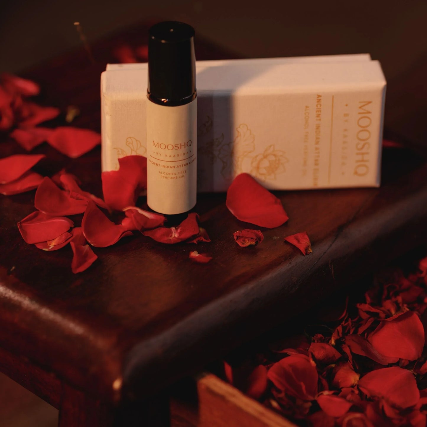 Mooshq perfume oil with red rose petals on a wooden surface