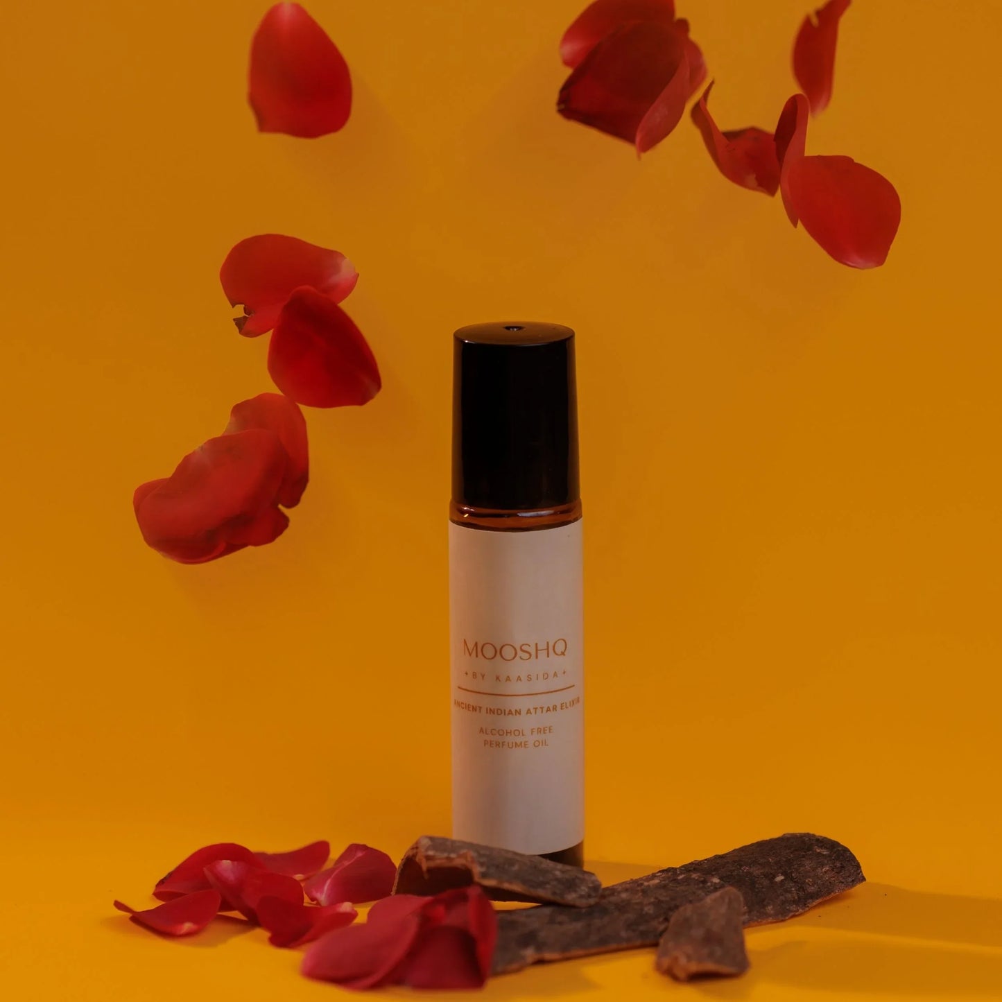 Mooshq perfume oil bottle with red rose petals on an orange background