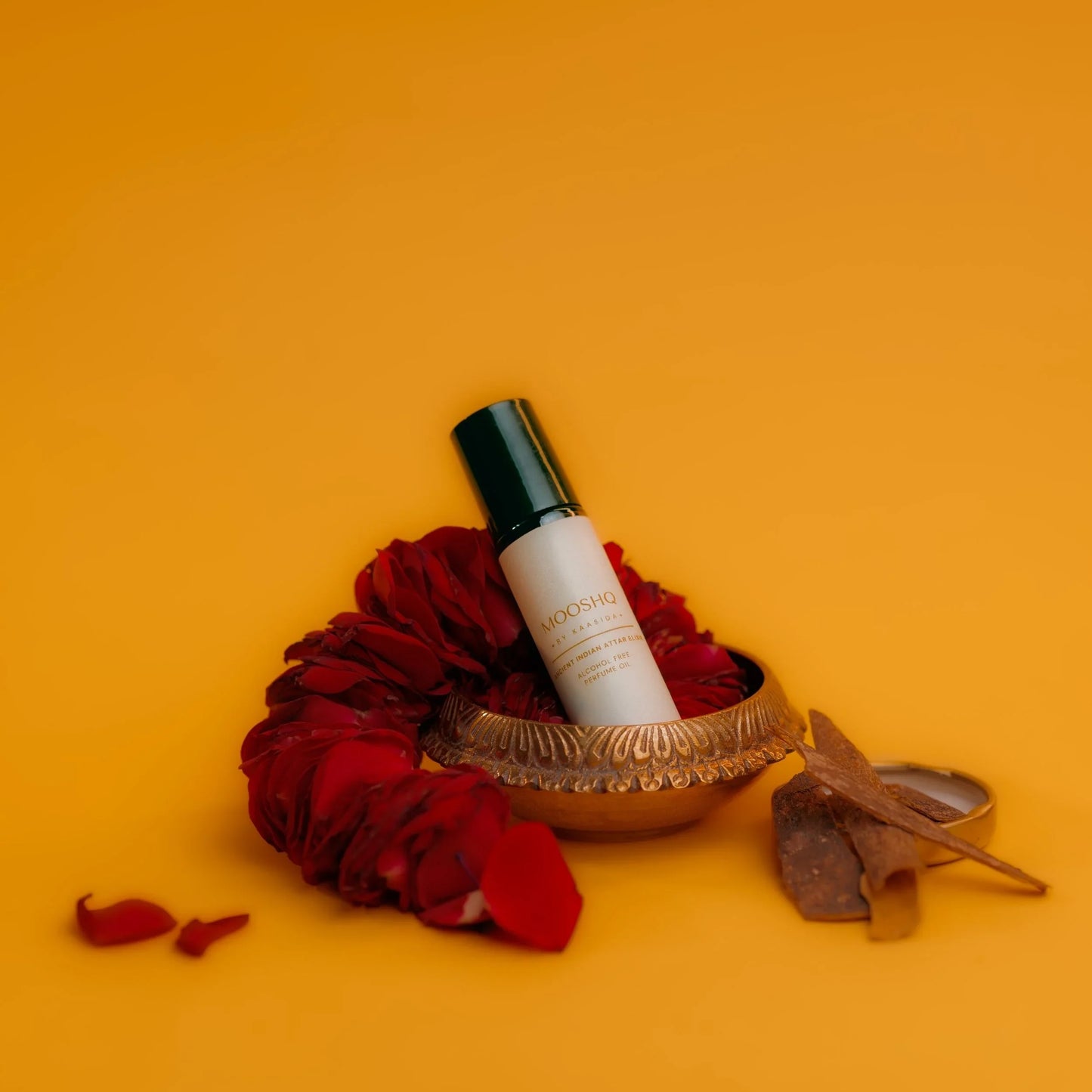 Perfume oil bottle with red rose petals and decorative elements on a yellow background