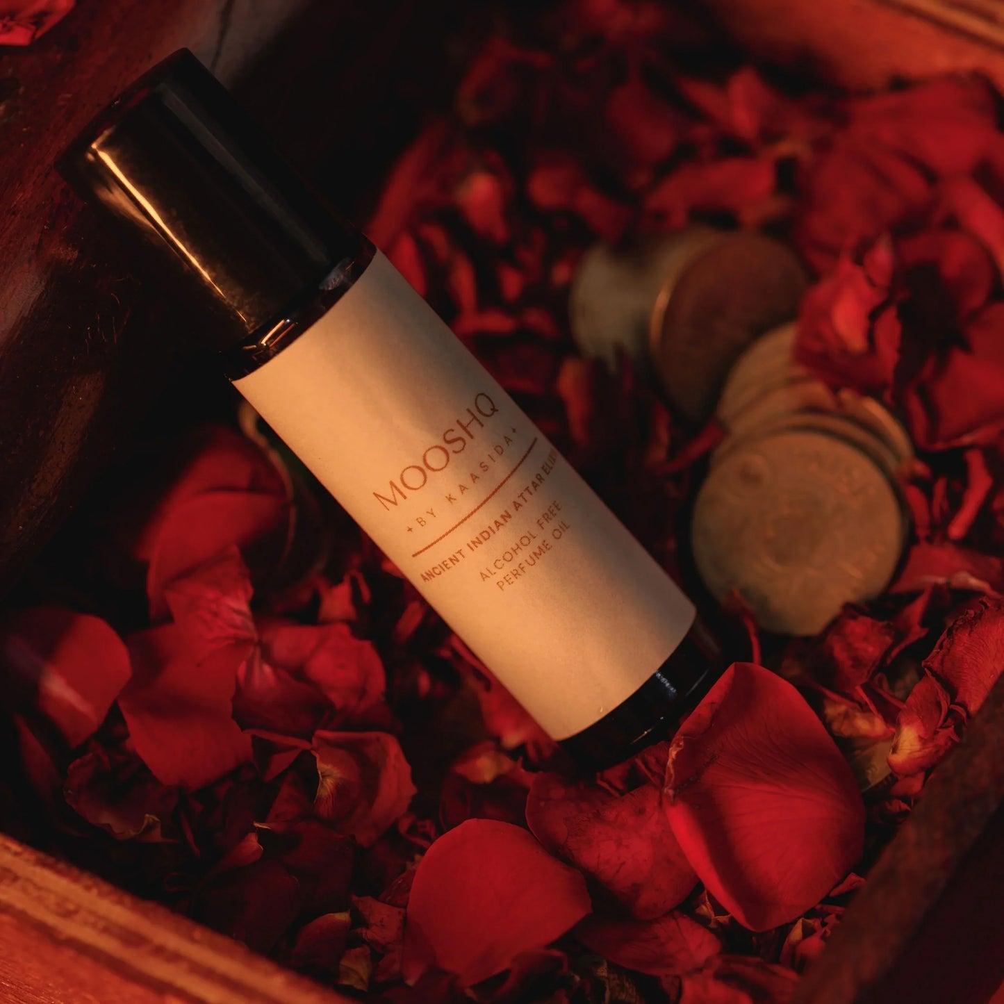 Perfume Oil bottle labeled 'Mooshq' on red rose petals