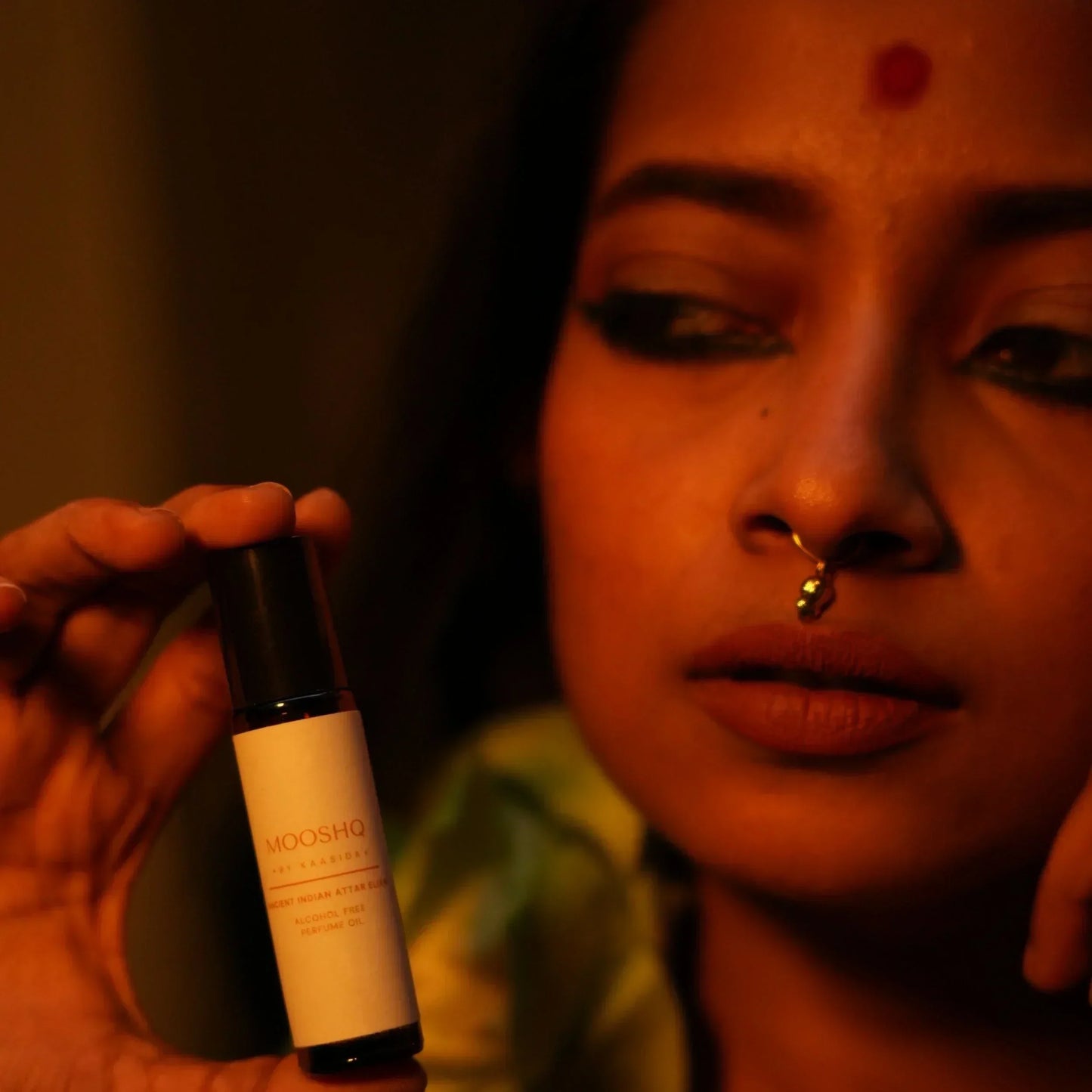 Woman holding Mooshq Perfume Oil against a blurred background