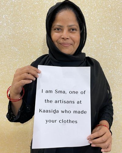 A female artisan holding up a banner that says "I am Sma, one of the artisans at Kaasida who made your clothes'.