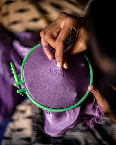 A person performing hand embroidery on a purple fabric