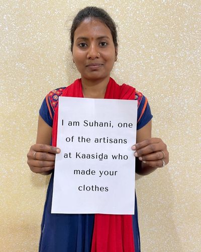 A female artisan holding up a banner that says "I am Suhani, one of the artisans at Kaasida who made your clothes'.