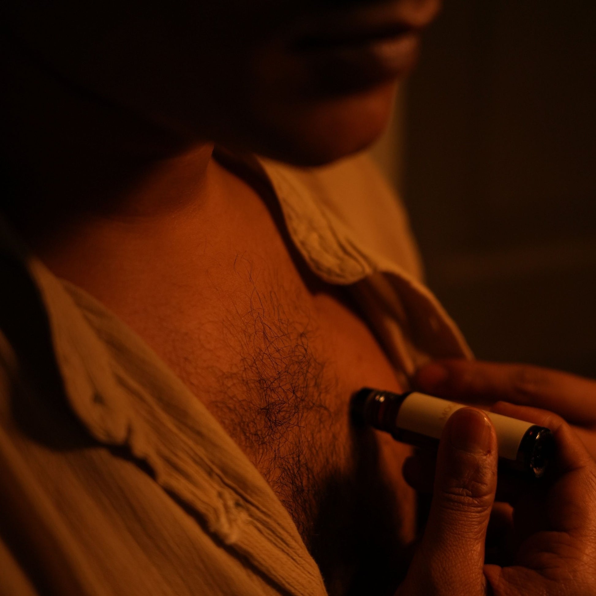 A man applying Mooshq Perfume Oil on his chest against a dark background