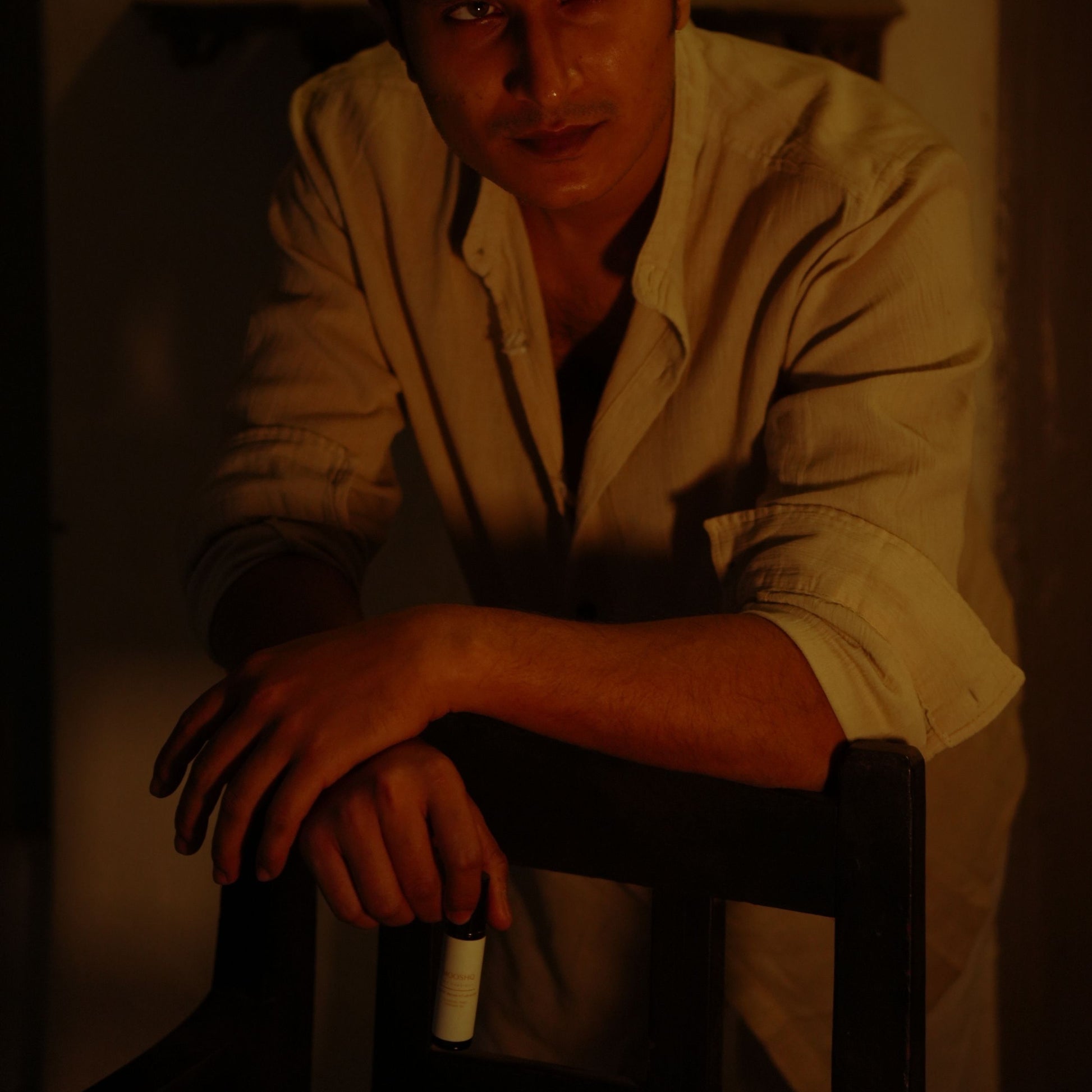 A man standing behind a chair with a dark background holding his Mooshq Perfume il