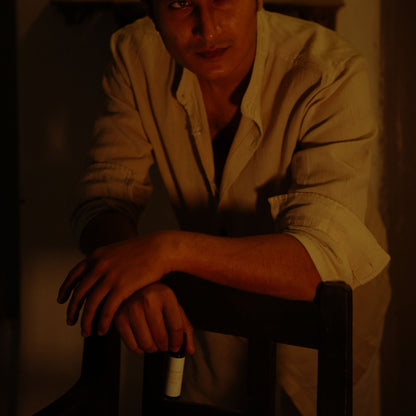 A man standing behind a chair with a dark background holding his Mooshq Perfume il