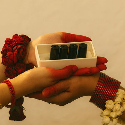 Hands holding a white box with perfume oil bottles, surrounded by red and white flowers on a beige background.