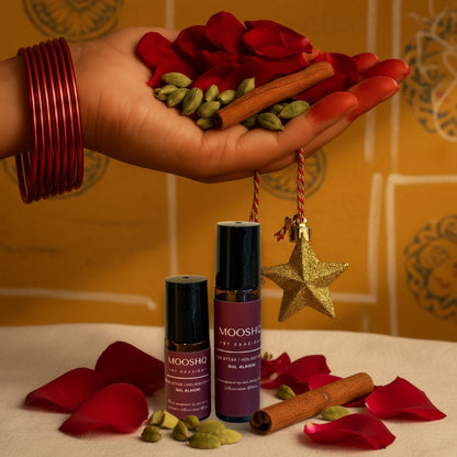 Hand holding red rose petals, green cardamom pods, and cinnamon sticks with Mooshq perfume oil on a yellow background.