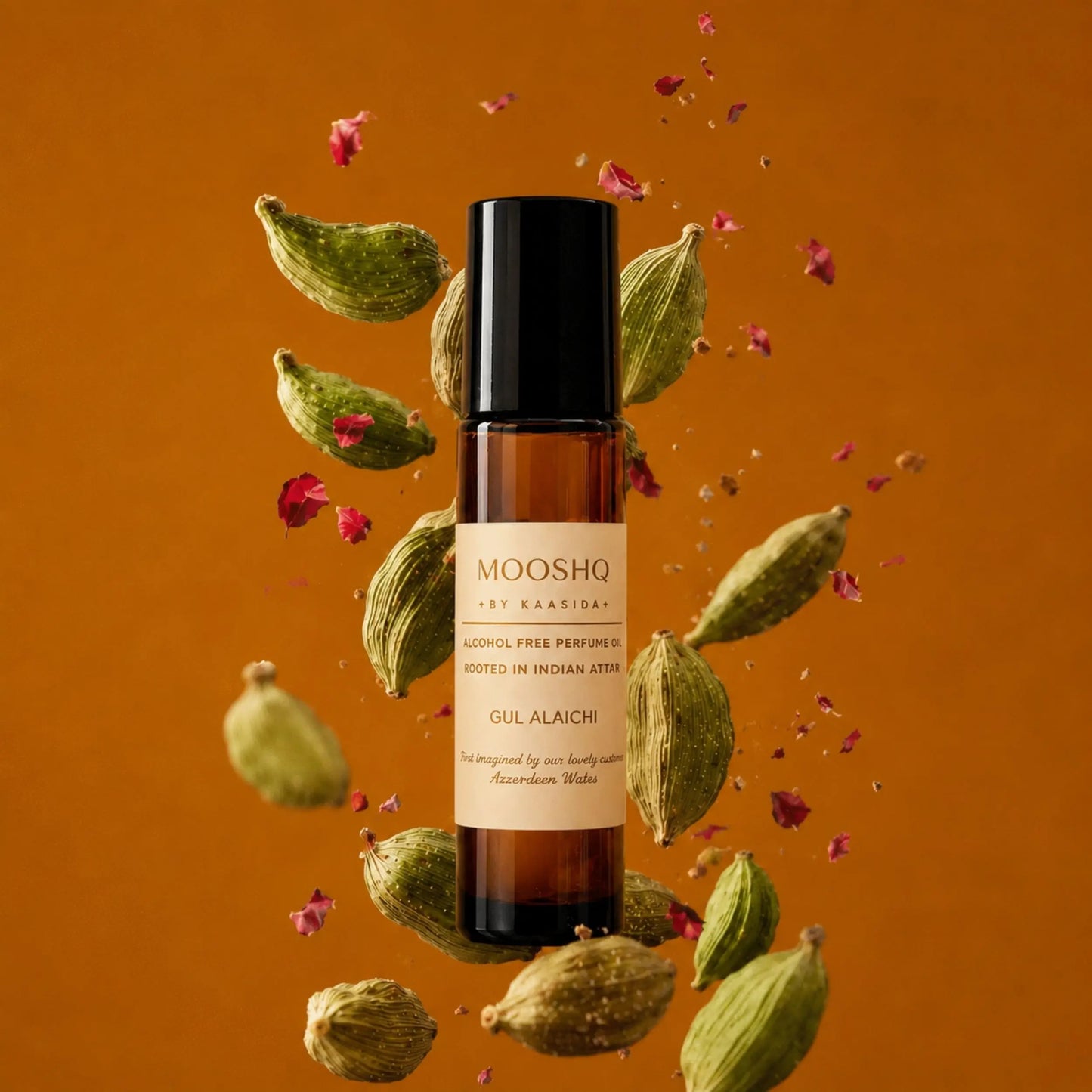 Mooshq perfume bottle with cardamom pods and rose petals on an orange background