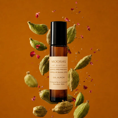 Mooshq perfume bottle with cardamom pods and rose petals on an orange background