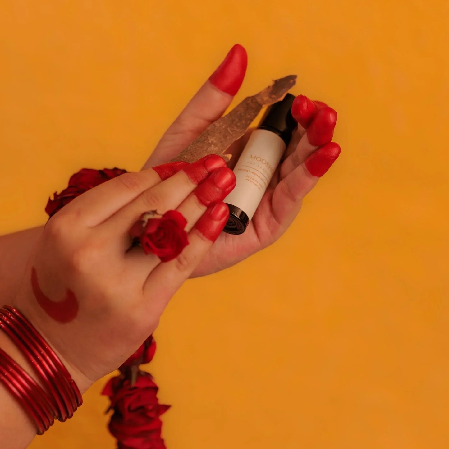 Hand with red nail polish holding a perfume oil bottle against an orange background