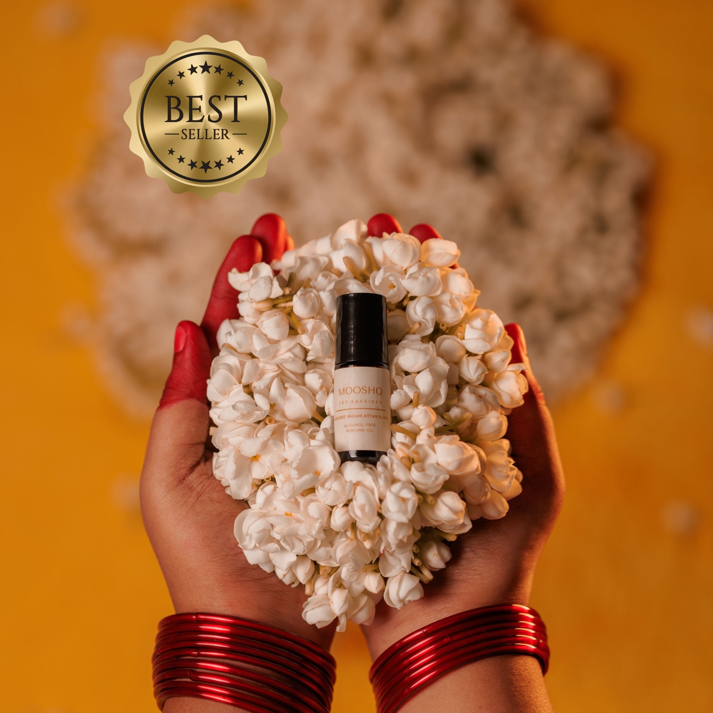 Hand holding a heart-shaped arrangement of JASMIN FLOWERS with a bottle in the center, against an orange background.