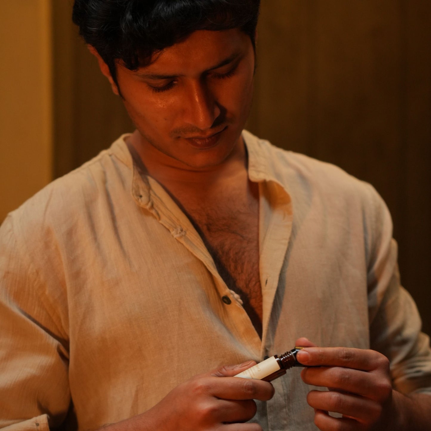 Man holding a Mooshq Perfume Oil with a warm-toned background