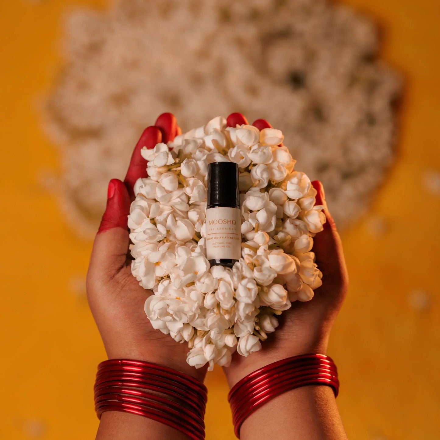 Hand holding a Jasmin flowers with a perfume oil bottle in the center against an orange background