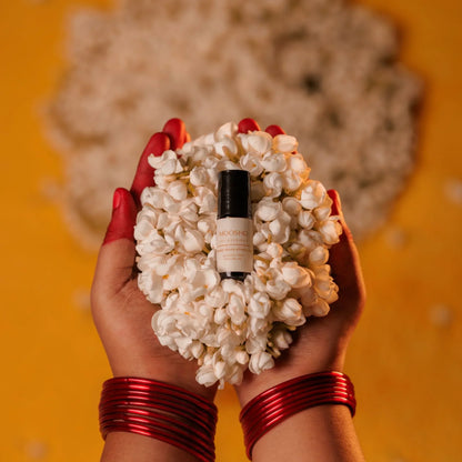 Hand holding a Jasmin flowers with a perfume oil bottle in the center against an orange background