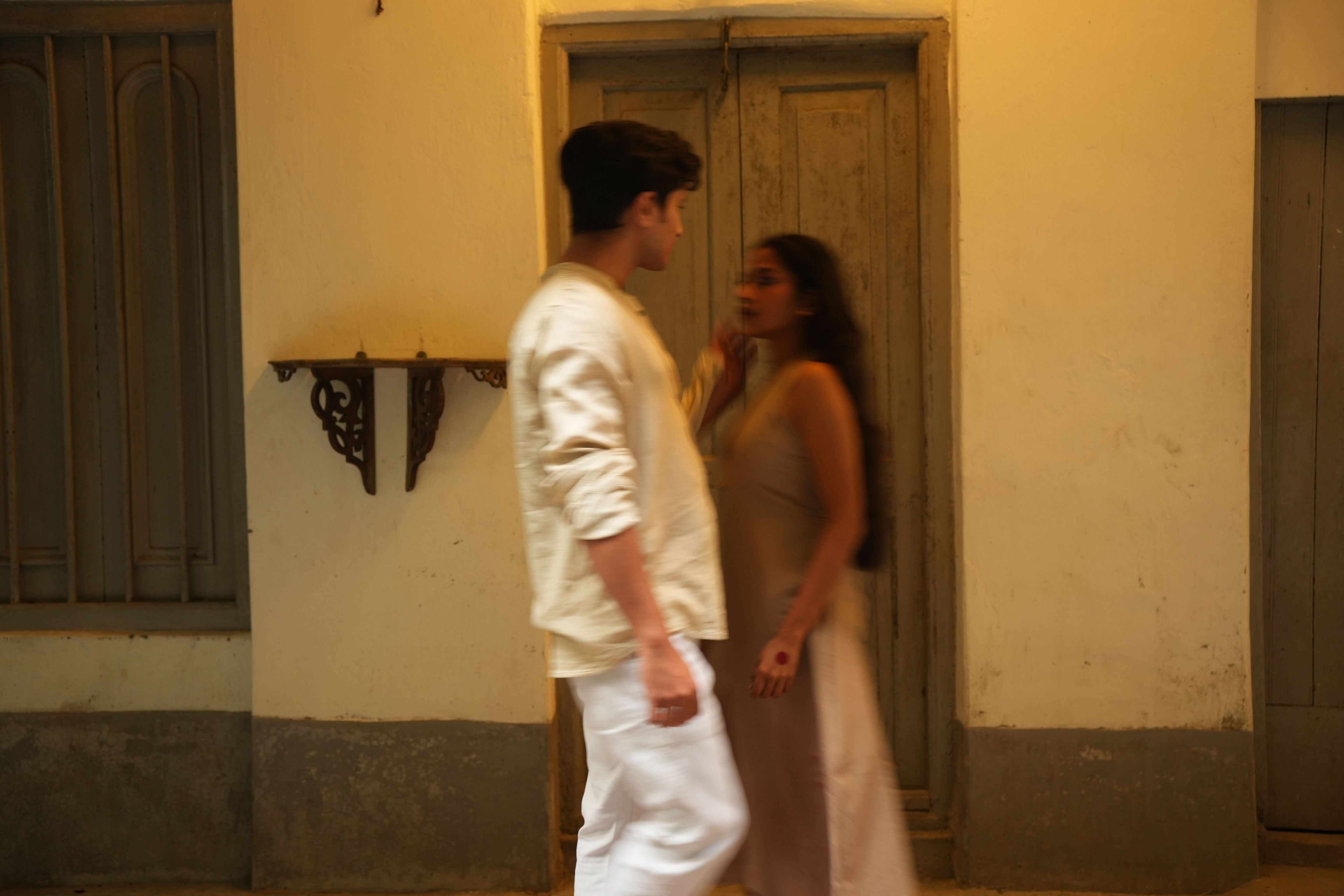 A man and a woman standing in a narrow alleyway with a building wall behind them 