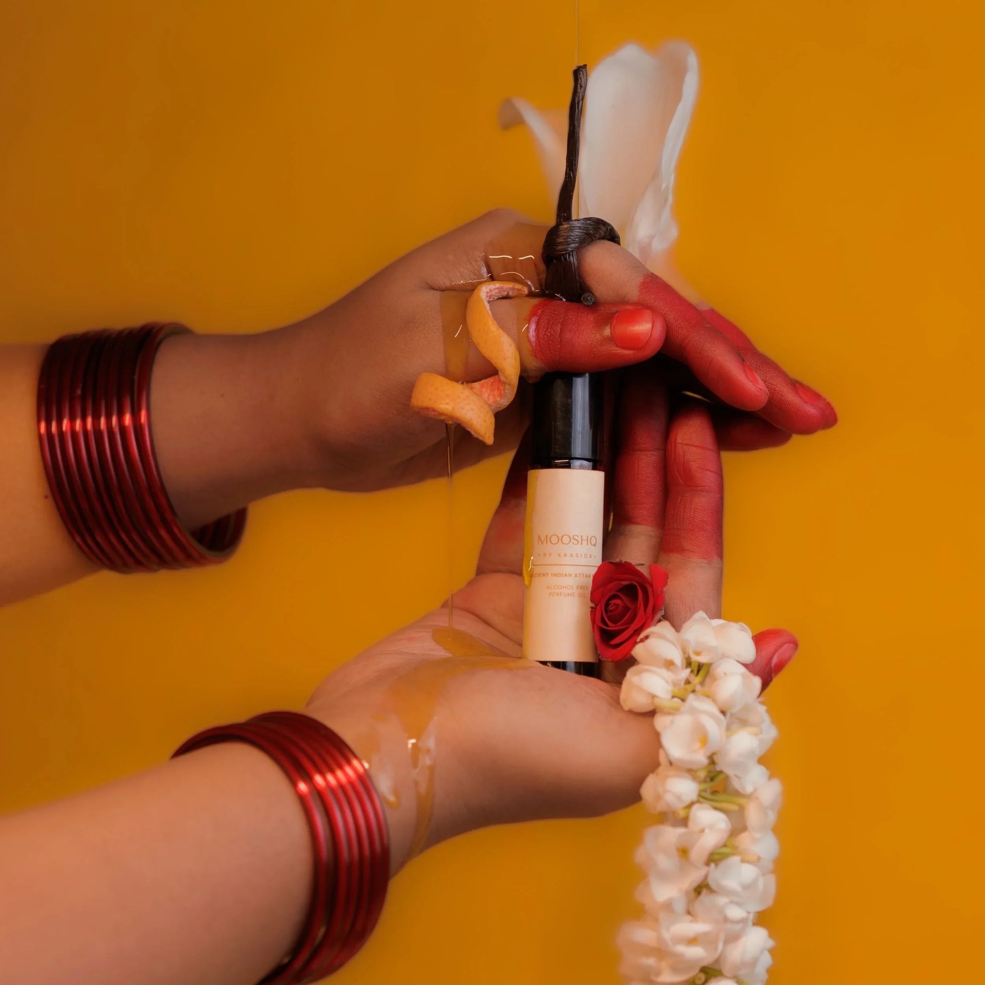Hands with red bangles holding a perfume oil bottle against a yellow background