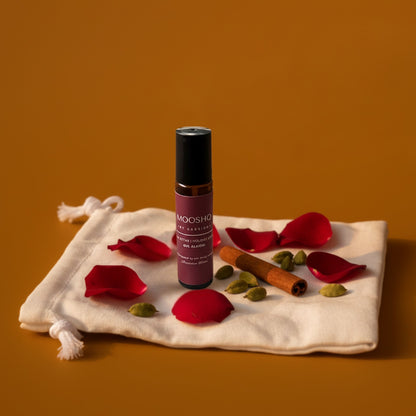 Mooshq Perfume Oil with red rose petals and cinnamon sticks on a fabric pouch against an orange background