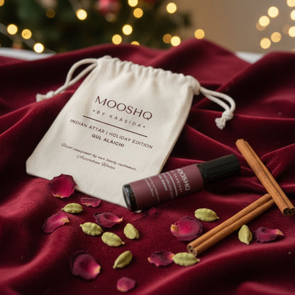 Mooshq by Kaasida Indian Attar Holiday Edition on a red fabric with cinnamon sticks and rose petals.