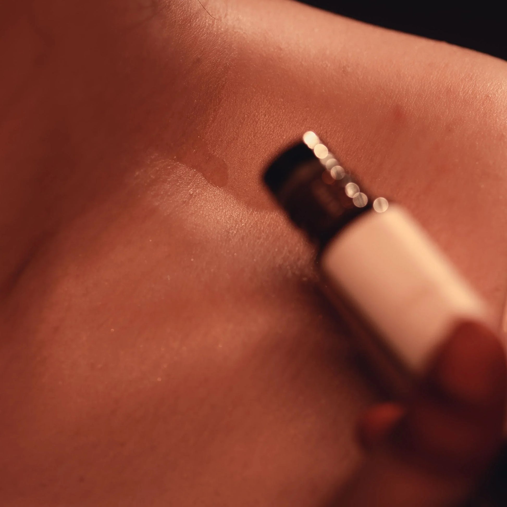 Close-up of a hand holding a bottle applying perfume oil  to skim