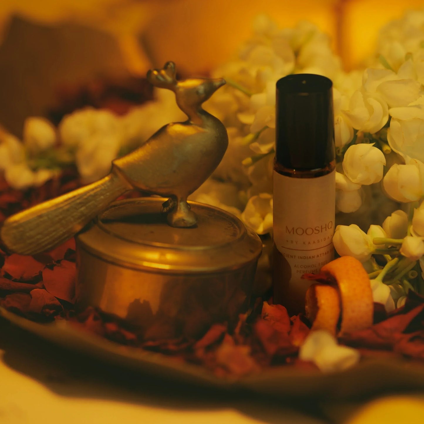 Mooshq perfume Oil bottle on a decorative tray with flowers and a bird figurine.