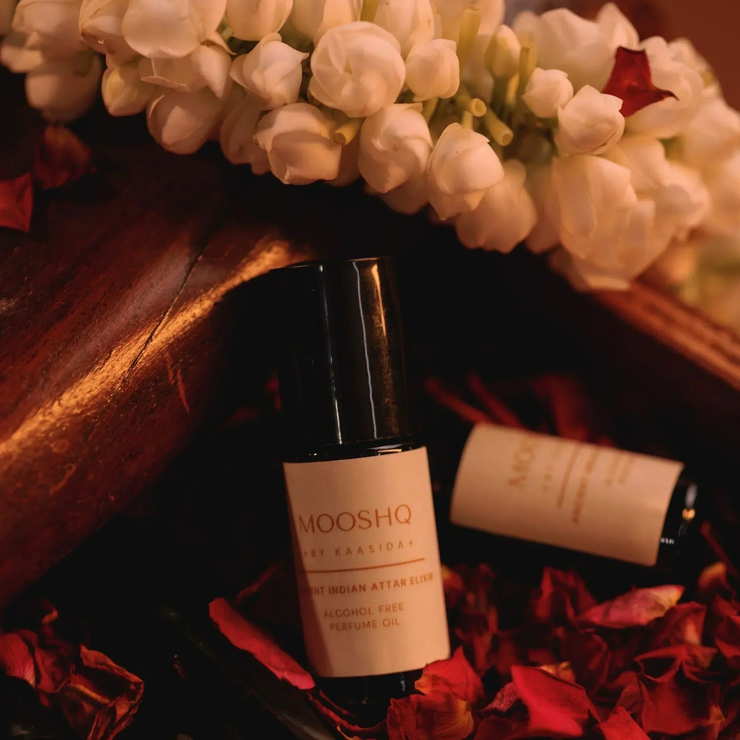 Mooshq perfume bottle on a wooden surface with flowers and petals