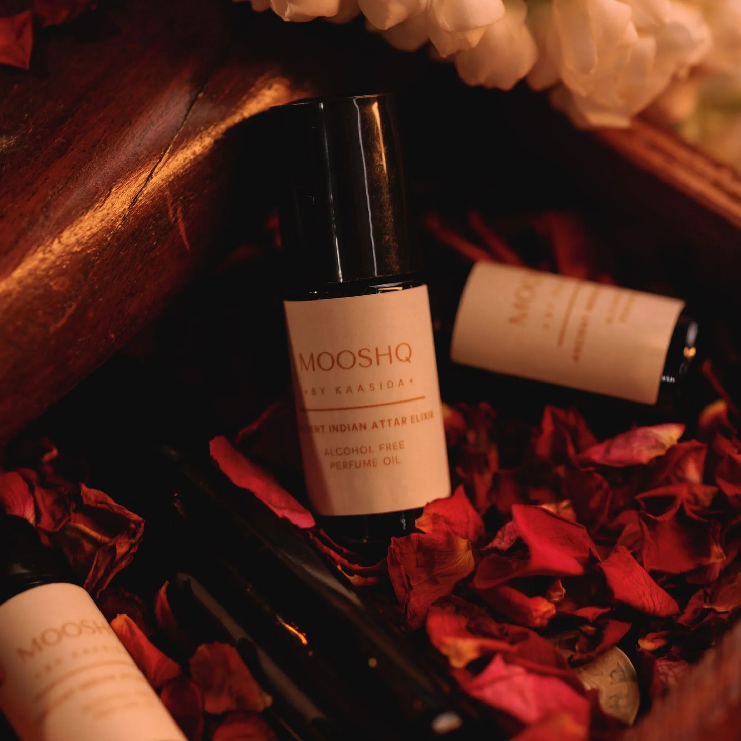 Mooshq perfume bottles on a wooden surface with red petals