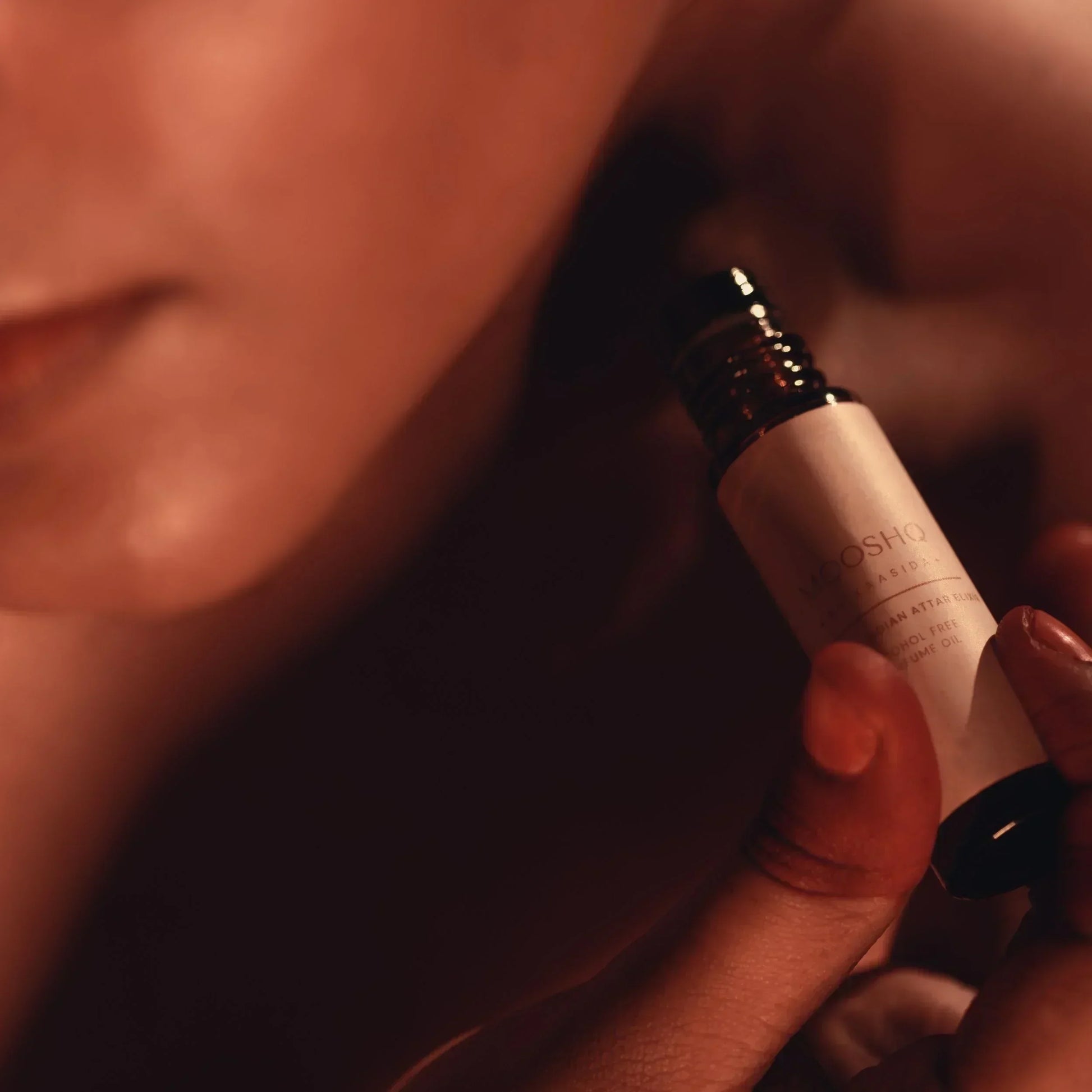 Close-up of a woman holding a perfume oil bottle with a blurred background