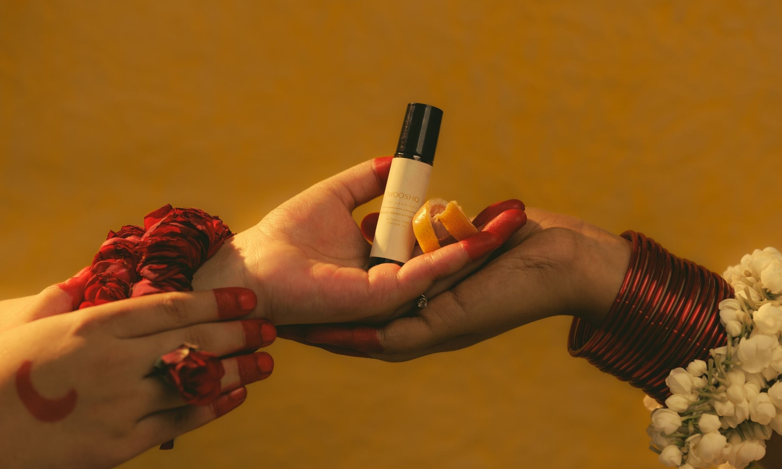 Two hands holding a small perfume oil bottle bottle with a yellow object against a warm-toned background