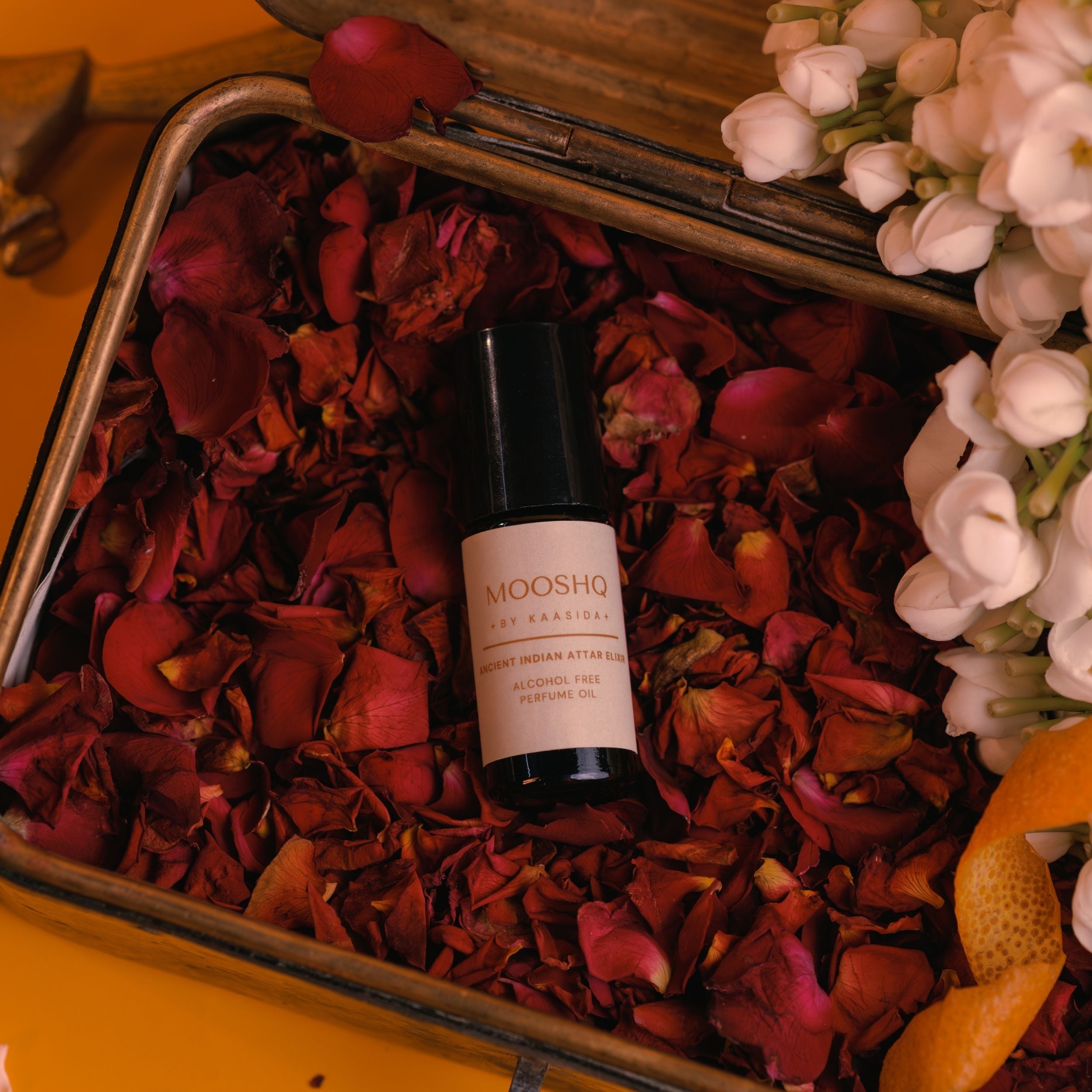 Mooshq perfume perfume oil bottle on rose petals with flowers and a box in the background
