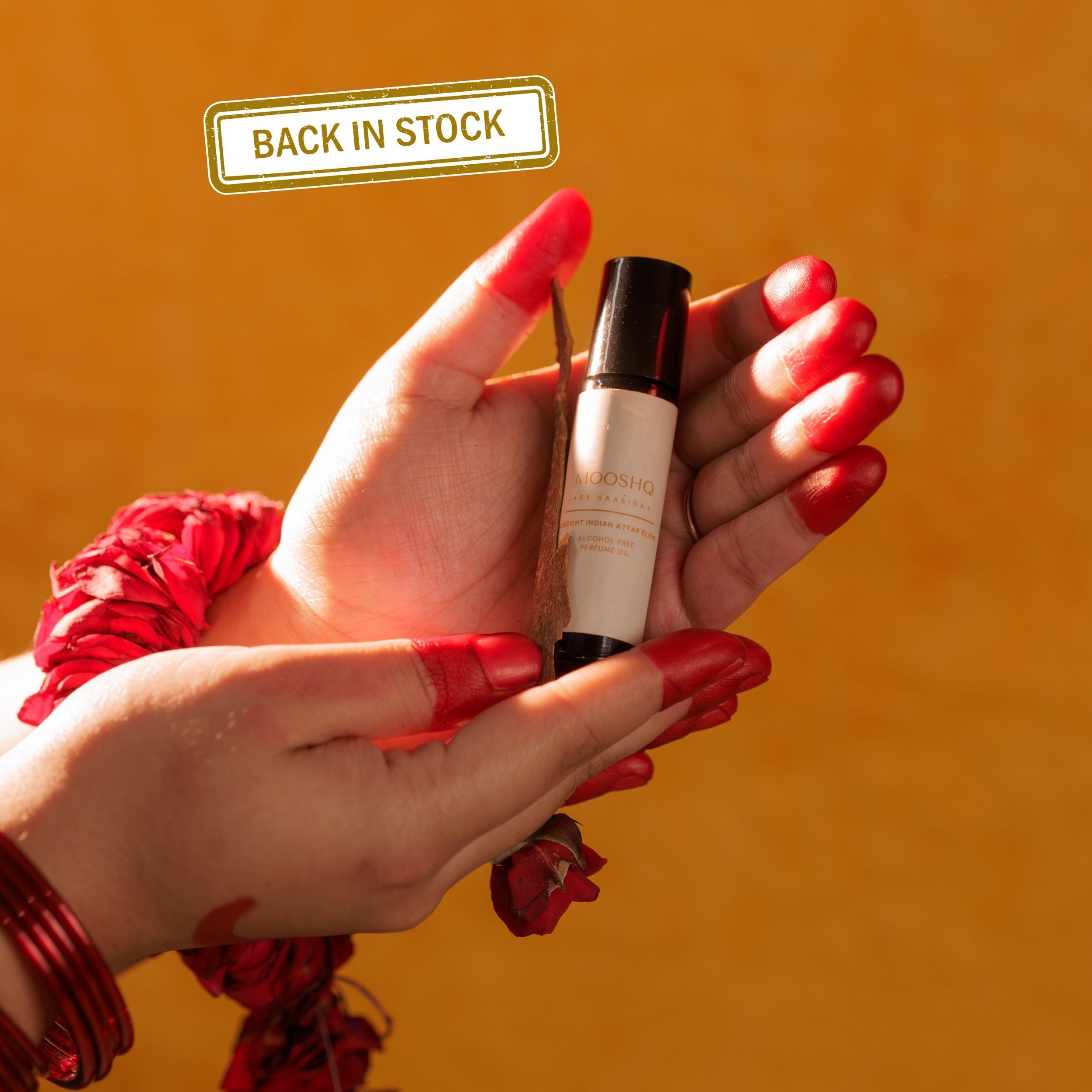 Hand holding a PERFUME OIL with 'Back in Stock' label on an orange background