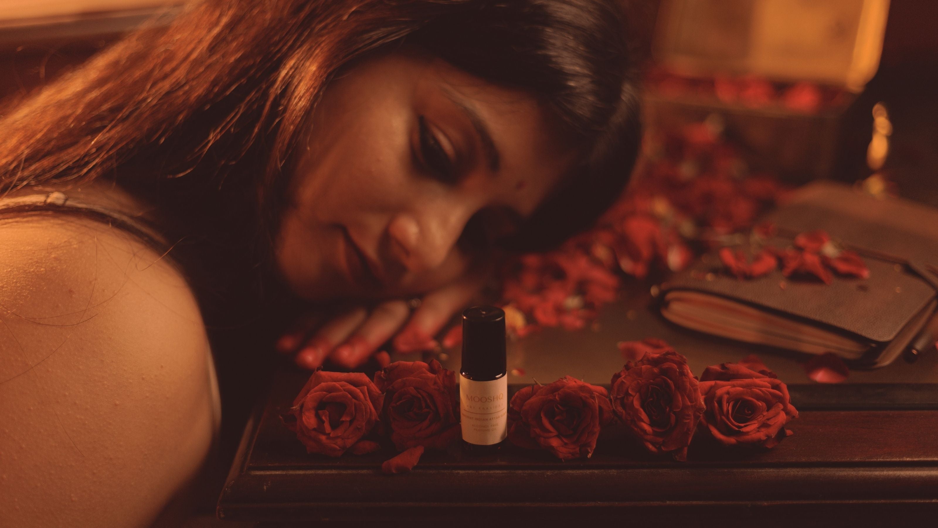 Woman lying on a bed with red roses and a perfume oil bottle e in a warm-toned setting