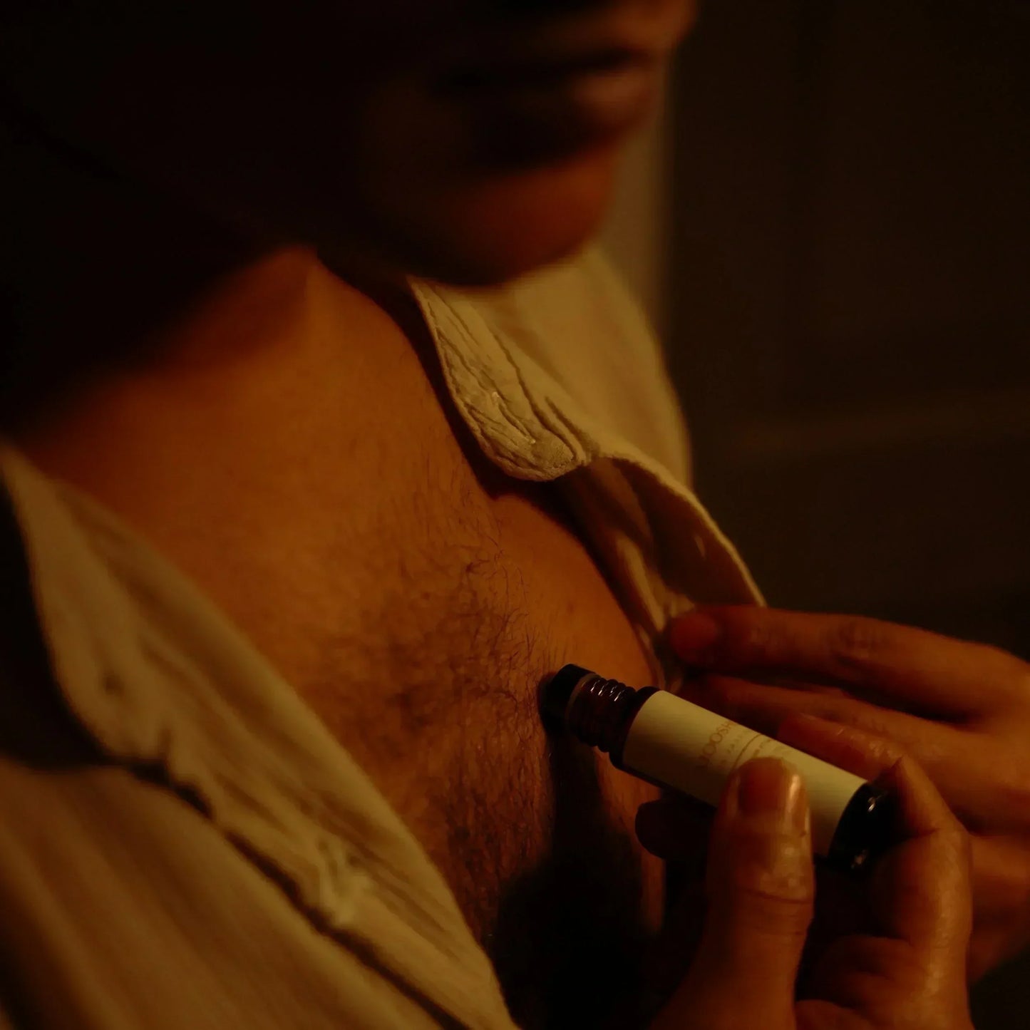 A man applying a perfume oil to his chest with a dark background