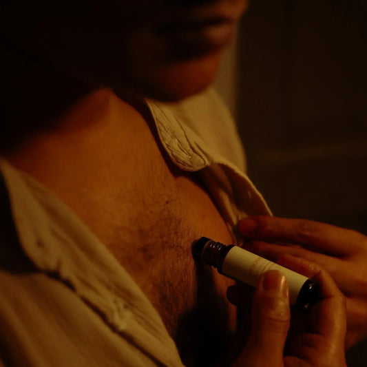 A man applying a perfume oil to his chest with a dark background