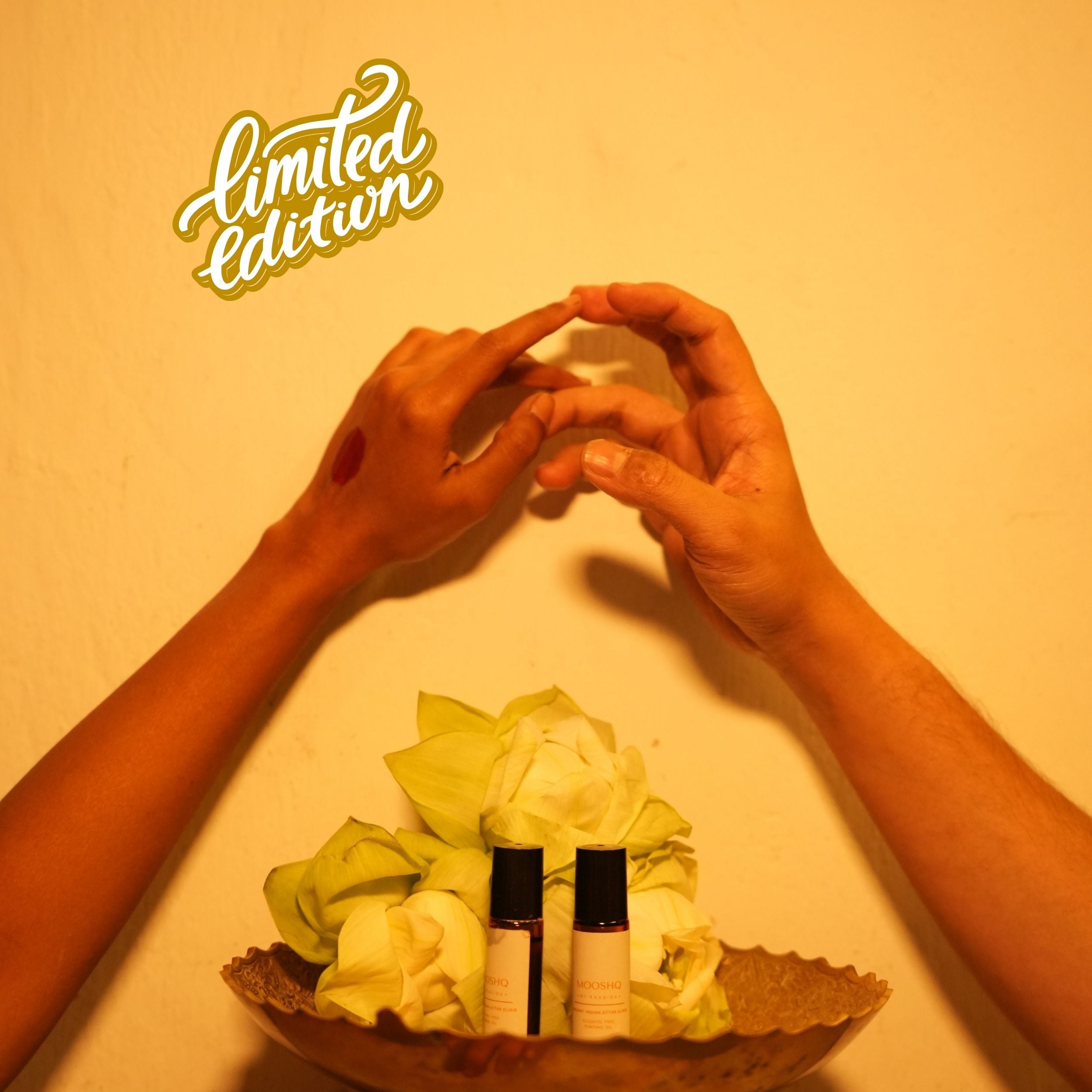 Two holding hands over lotus flowers and two black Mooshq Perfume Oil against a yellow background, with 'limited edition' text.