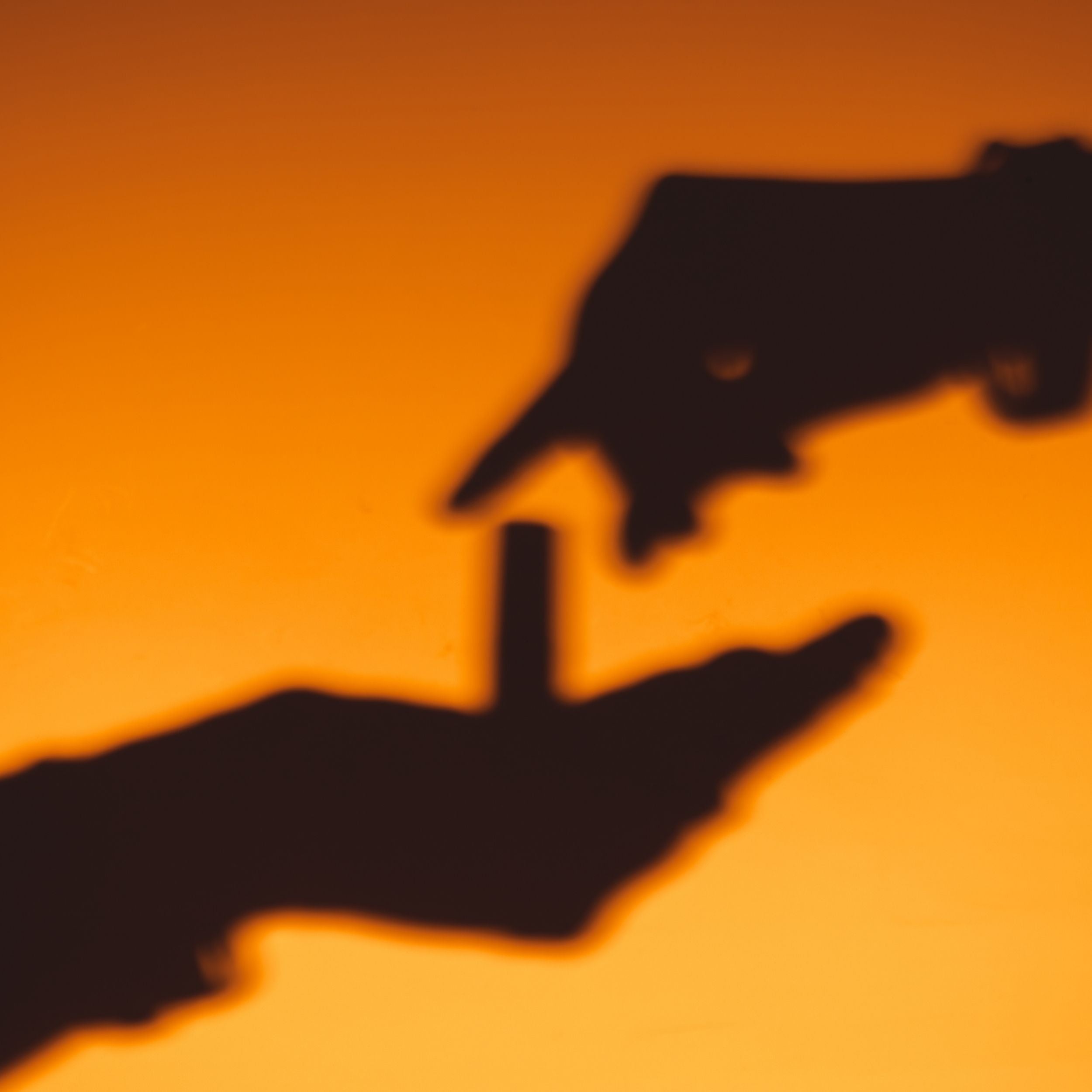 Shadow of a hand holding a perfume oil with another hand reaching out against an orange background