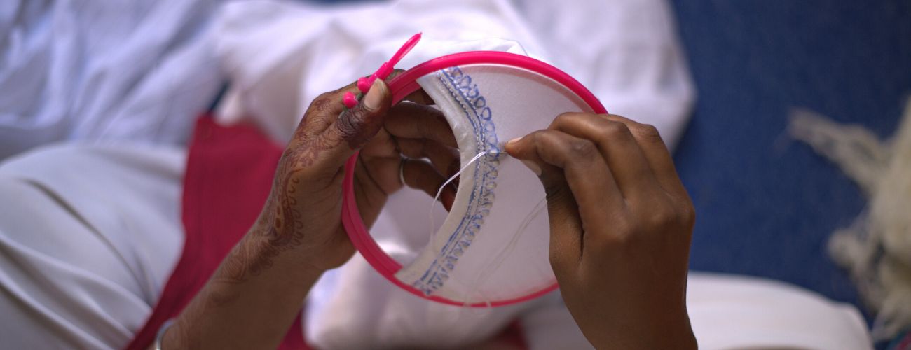 A person's hand performing embroidery on a white fabric