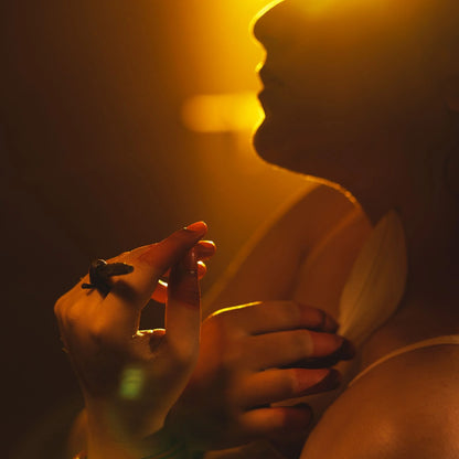 woman holding a lily petal and perfume oil with a warm, blurred background