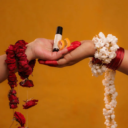 Two hands holding Mooshq perfume oil bottle and decorative items against an orange background