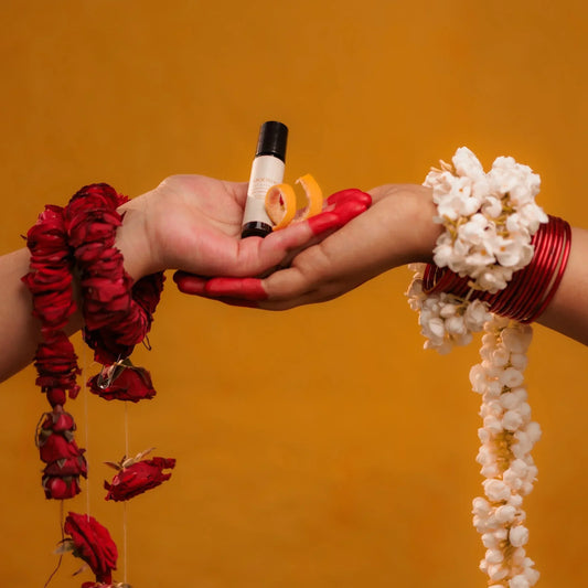 Two hands holding Mooshq perfume oil bottle and decorative items against an orange background