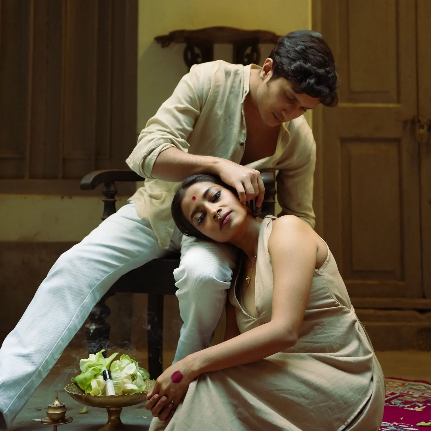 Two people in traditional attire sitting together in a warm-toned room applying Mooshq Perfume oil on each other