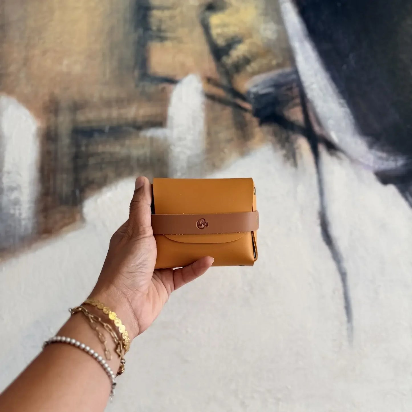 Hand holding a mustard yellow vegan leather perfume oil pouch with brown strap against a blurred background