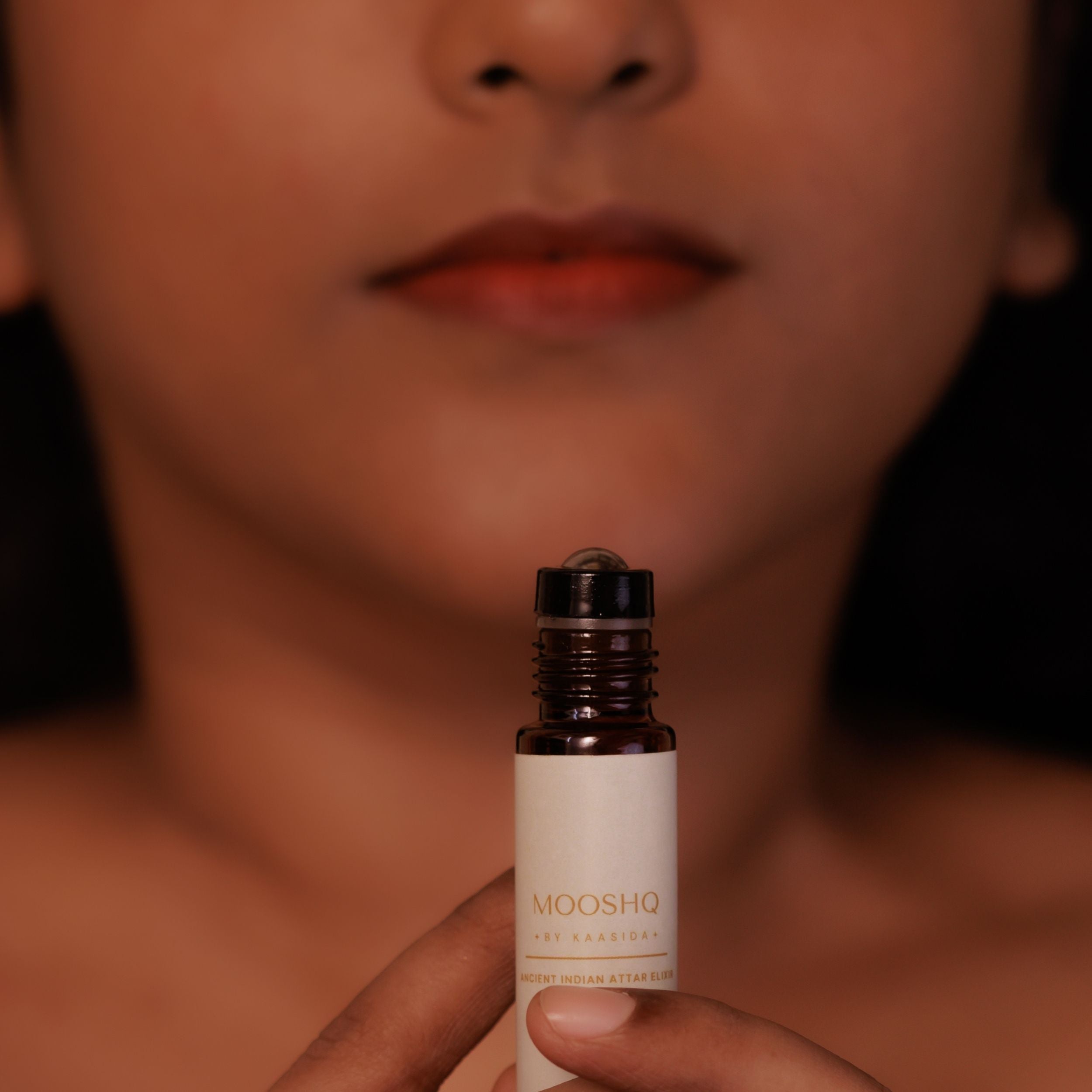 Woman holding a Mooshq perfume oil bottle with a blurred background