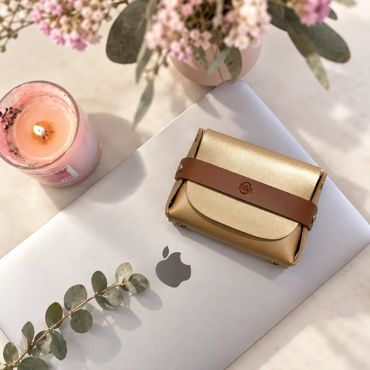 Gold pouch with brown strap on a laptop next to a burning candle