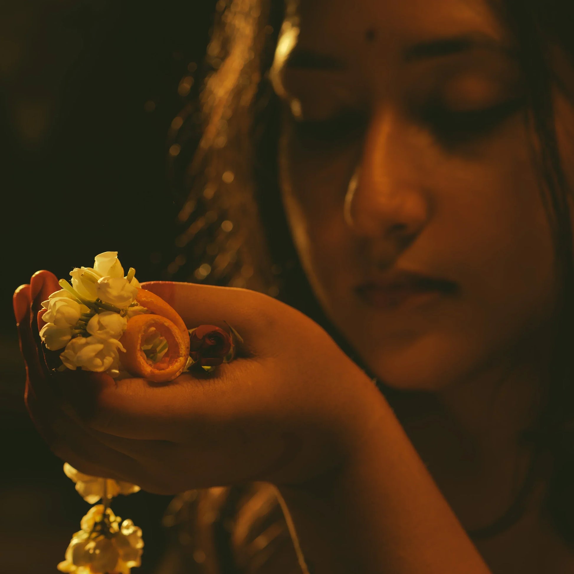 woman holding small flowers with a warm, dark background